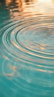 Tranquil water surface with golden sunset reflections creating circular ripples and waves in turquoise blue pool or lake for relaxation and wellness concepts.