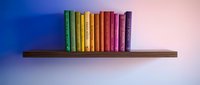 Colorful rainbow books arranged on wooden shelf against gradient background for education, library, reading and learning concepts.