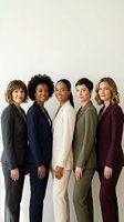 Five diverse women in professional business attire standing together against neutral background, representing corporate teamwork, leadership and workplace diversity for business communications.