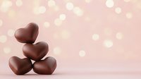 Dark chocolate hearts stacked in pyramid shape against soft pink bokeh background with copy space, romantic food photography for Valentine's Day and love concepts.