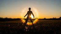 Young woman meditating in lotus position at sunset in grassy field with dramatic sunburst rays creating spiritual atmosphere for wellness and mindfulness content.