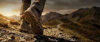 Hiker boots stepping on rocky mountain trail during golden hour sunrise with dramatic landscape and rugged terrain in background for outdoor adventure concepts.