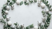 Flat lay arrangement of white and silver ornaments with eucalyptus branches forming a circular frame on light background, suitable for holiday greeting cards and seasonal designs.