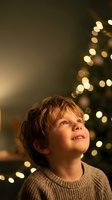 Young boy looking up with wonder at Christmas tree lights creating magical holiday atmosphere with warm bokeh background for seasonal campaigns.