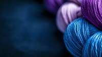 Vibrant merino wool yarn balls in purple and turquoise tones against dark background, showing detailed fiber texture and twist pattern for knitting and crafting projects.