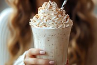 Creamy coffee beverage topped with whipped cream and caramel drizzle, held by a woman with manicured nails. Perfect for cafes, restaurants, and beverage marketing.