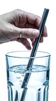 Hand inserting a reusable metal straw into a clear glass of water, showing light refraction effect on white background.