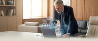Senior Caucasian businessman in dark suit working on laptop with digital technology icons overlay in modern office environment for corporate presentations.