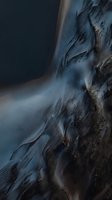 Aerial view of dramatic coastline with flowing water patterns creating abstract natural formations along sandy beach and dark ocean waves.
