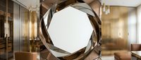 Modern twisted metal sculpture with circular opening displayed in contemporary interior space with glass partitions and warm lighting.
