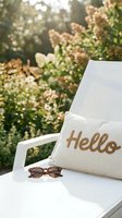 White outdoor lounge chair with a linen hello embroidered pillow and sunglasses in a sunny garden setting, warm summer lifestyle mood.