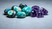 Collection of polished gemstones including labradorite and amethyst crystals arranged on gray surface for jewelry making and healing practices.