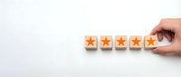 Hand placing wooden blocks with orange stars showing five star rating system for customer feedback and quality assessment on white background.