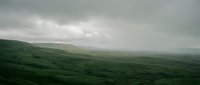 Lush rolling green hills under dramatic overcast sky with misty atmospheric conditions, suitable for landscape and nature backgrounds.