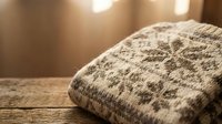 Cozy knitted wool sweater with traditional Nordic pattern folded on wooden surface in warm sunlight creating comfortable autumn winter atmosphere.