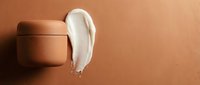 Cream or lotion sample smeared on terracotta background next to cosmetic jar, showcasing skincare product texture and consistency for beauty and wellness marketing.