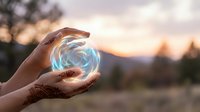 Hands holding glowing energy sphere with swirling light effects against sunset mountain landscape background for spiritual and mystical concepts.