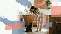 Young woman in beige casual wear feeding black cat in modern kitchen with colorful geometric wall art and wooden cabinets for pet care lifestyle content.