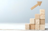 Wooden blocks arranged as ascending stairs with arrow pointing upward on light background, representing growth, success and business development progress.