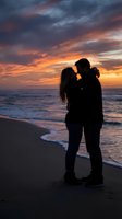 Romantic couple silhouette embracing on beach at sunset with dramatic orange and purple sky reflecting on ocean waves for love and relationship concepts.