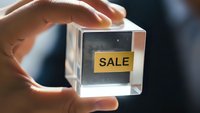 Hand holding transparent glass cube with yellow sale label inside for marketing and promotional campaigns in retail business.