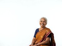 Senior woman with gray hair and glasses wearing traditional Indian sari in gold and burgundy tones, smiling warmly against white background. Portrait suitable for healthcare, wellness, diversity and inclusion projects.