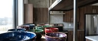 Modern kitchen with colorful glass vessel sinks in blue, green, and red tones displayed on counter, stainless steel appliances and wooden cabinetry visible in background for interior design and home decor projects.