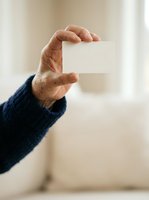 Senior male hand holding blank white card against neutral background, ideal for business contact information, promotional messaging, or corporate branding applications.