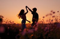 Romantic couple silhouettes dancing in wildflower field at golden sunset creating heart shape with arms for love and relationship concepts.