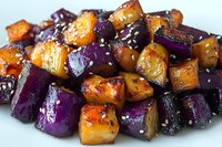 Roasted purple and orange sweet potato cubes garnished with sesame seeds on white plate, close up view of colorful vegetarian side dish with glazed finish.