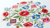 Traditional folk art embroidery with colorful floral motifs featuring red poppies, blue cornflowers and green leaves on white fabric for craft projects.