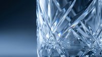 Crystal glassware with intricate cut patterns and light refractions against blue background, suitable for luxury product photography and tableware design projects.