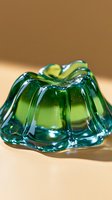 Green translucent jelly dessert with wavy ridged surface catching light and creating glossy reflections against neutral background, macro food photography.