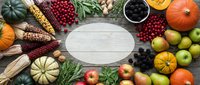 Autumn harvest vegetables and fruits arranged around empty wooden plate on rustic table with pumpkins, corn, cranberries, apples creating seasonal food frame.