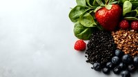 Fresh organic superfoods arranged on light gray background - strawberries, blueberries, raspberries, black quinoa, granola and baby spinach leaves for healthy eating.