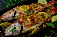 Fresh whole red snapper garnished with grilled lemon slices, herbs and parsley on dark background. Mediterranean seafood cuisine prepared for restaurant serving.