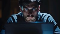 Young Caucasian man with intense blue eyes illuminated by laptop screen in dark room, dramatic lighting creates mysterious atmosphere for cybersecurity and hacking concepts.