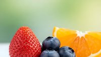 Fresh mixed berries and orange slice on soft green background for healthy eating and nutrition concepts.