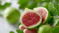 Fresh ripe figs cut in half showing pink flesh with seeds, green leaves with water drops, healthy organic fruit for cooking and nutrition concepts.