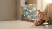 Hands holding transparent tablet displaying holographic digital interface with floating icons and data visualization for futuristic technology concepts.