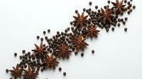 Star anise and allspice berries arranged in diagonal line on white background for culinary, food styling and spice trade design projects.