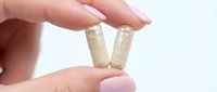 Hand holding two beige capsules or pills between fingers on white background for healthcare and pharmaceutical supplement concepts.