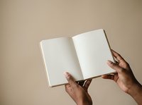 Open blank notebook held by hands against neutral beige background, suitable for publishing, education, journaling, and creative writing projects.