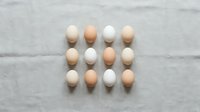 Fresh organic eggs in brown and white varieties arranged in neat rows on rustic linen fabric background for cooking and baking concepts.