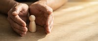 Protective hands shielding wooden figure on desk symbolizing care, security, insurance coverage, employee protection and business safety concepts.