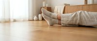 Woman in cozy socks relaxing on wooden floor next to moving boxes in bright home interior during relocation day.