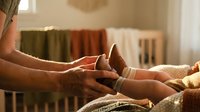 Loving parent gently holding newborn baby feet in warm nursery setting with soft natural lighting and cozy atmosphere for family bonding moments.