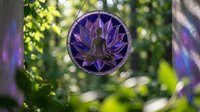 Purple lotus meditation mandala suncatcher hanging in garden with natural bokeh light creating peaceful zen atmosphere for spiritual wellness and mindfulness practice.