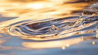 Mesmerizing water drop splash creating concentric ripples on liquid surface with golden sunset reflections, capturing motion and tranquility in nature.