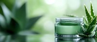 Glass jar with green cosmetic cream and fresh aloe vera leaf on blurred natural background. Organic skincare and beauty product photography.